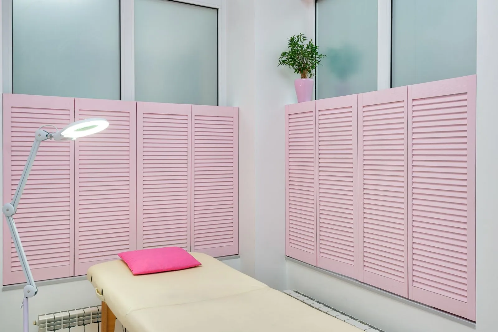 Interior of contemporary spa salon with couch under bright light of lamp with pink shutters on windows